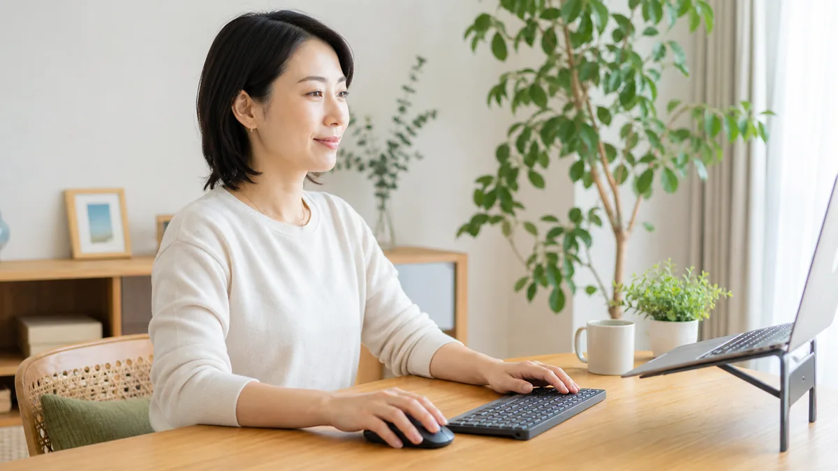 腕を机で支えながら、キーボードとマウスを近くに置いてパソコン作業をする女性